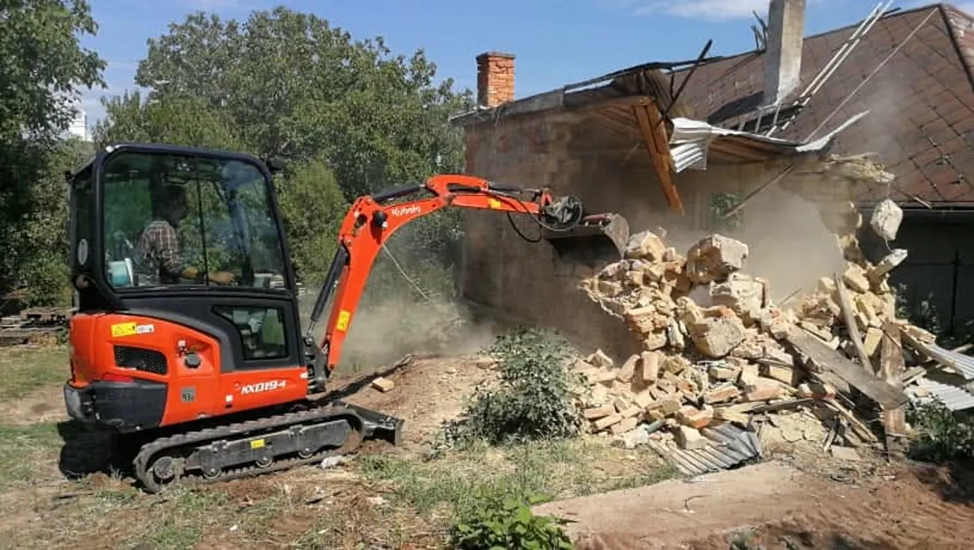 Kubota minikotró tégla melléképületet bont, törmelékhalom előtte.